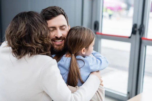 Hombre barbudo feliz abrazando a la familia en aeropuerto - foto de stock