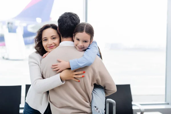 Cheerful woman and kid hugging man in airport — Photo de stock