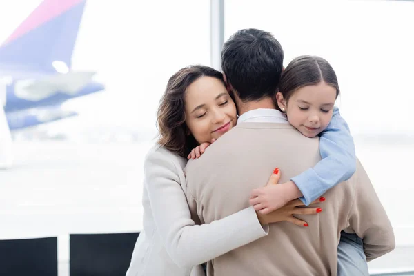 Happy woman and daughter hugging man in airport — Stock Photo
