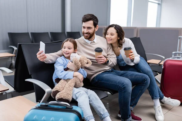 Feliz hombre tomando selfie con alegre familia en aeropuerto salón - foto de stock
