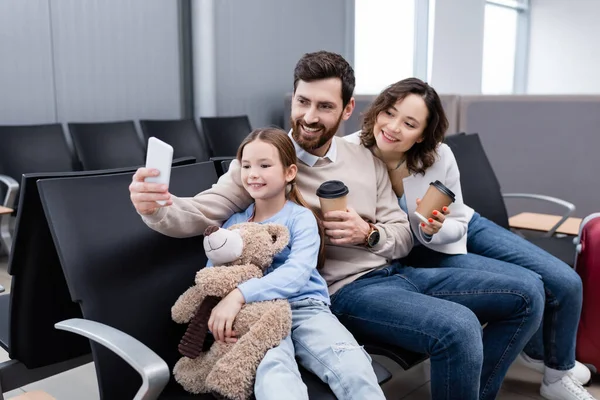 Щасливий чоловік бере селфі з веселою дружиною і дочкою в залі для аеропортів — стокове фото