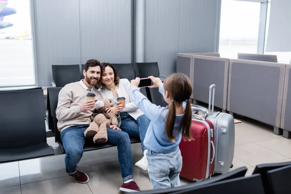 Kid taking photo of happy parents with paper cups in airport lounge — Stock Photo