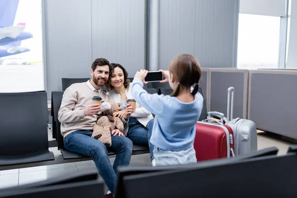 Girl taking photo of happy parents with paper cups in airport lounge — Stock Photo