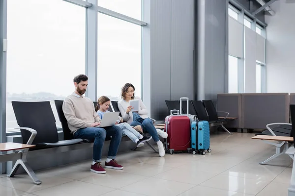 Сім'я використовує пристрої, сидячи в залі для аеропортів — стокове фото