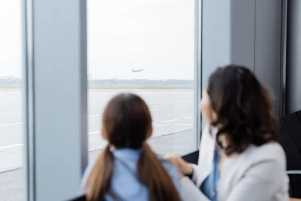 Mutter und Tochter blicken verschwommen durch Flughafenfenster auf startendes Flugzeug — Stockfoto