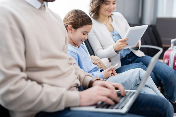 Cheerful kid using smartphone near blurred parents with gadgets — Fotografia de Stock