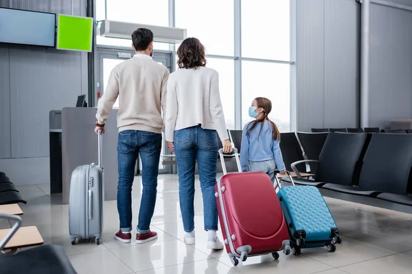 Kid in medical mask looking at parents in airport hall — Stock Photo