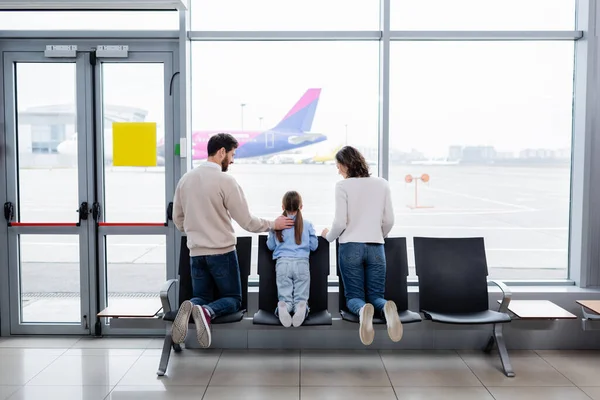 Батьки дивляться на дочку біля вікна в аеропорту — стокове фото