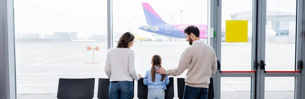 Padres mirando a la hija cerca de la ventana en el aeropuerto, pancarta - foto de stock