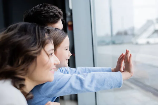 Vista lateral de la familia alegre mirando la ventana en el aeropuerto - foto de stock