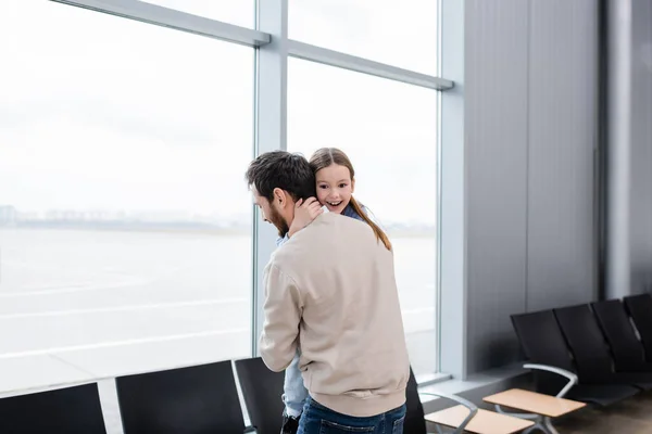 Fröhliches Kind umarmt bärtigen Vater am Flughafen — Stockfoto