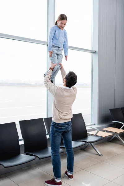 Father lifting happy daughter in airport lounge — стоковое фото