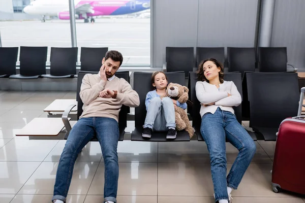 Bored man looking at watch near daughter and wife in airport — стокове фото