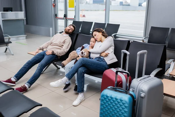 Hombre aburrido esperando con hija y esposa cerca de equipaje en el salón del aeropuerto - foto de stock