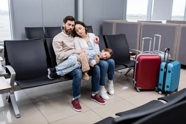 Kid sleeping on knees of tired parents in airport lounge - foto de stock