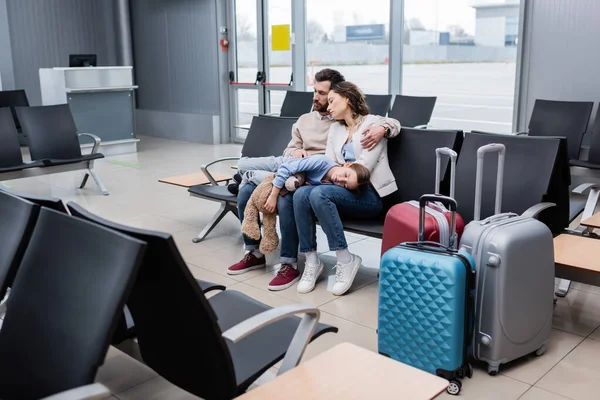 Girl sleeping on knees of tired parents in airport lounge — стоковое фото