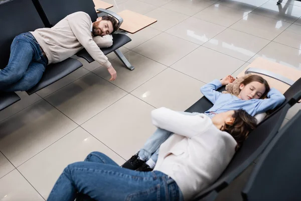 Vista de ángulo alto de la familia durmiendo en los asientos del aeropuerto en la sala de salida - foto de stock