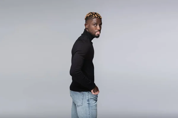 Young african american man with vitiligo looking at camera while standing with hand in pocket isolated on grey — Foto stock