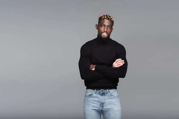 African american man with vitiligo, wearing black turtleneck and jeans, standing with crossed arms isolated on grey - foto de stock
