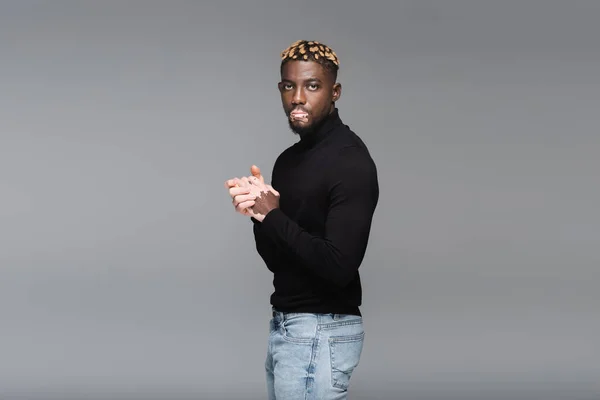 Stylish african american man with vitiligo, wearing jeans and black turtleneck, looking at camera isolated on grey — Photo de stock