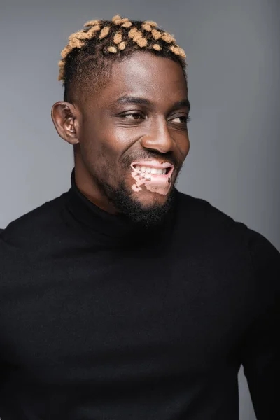 Happy african american man with vitiligo and trendy hairstyle looking away isolated on grey — Stock Photo