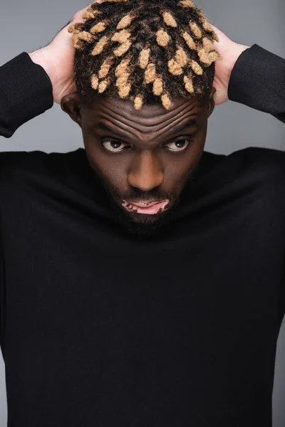 Young african american man with vitiligo and trendy hairstyle posing with hands behind head isolated on grey — Stockfoto