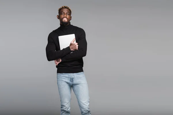 African american man with vitiligo, wearing black turtleneck and jeans, holding laptop isolated on grey — Foto stock