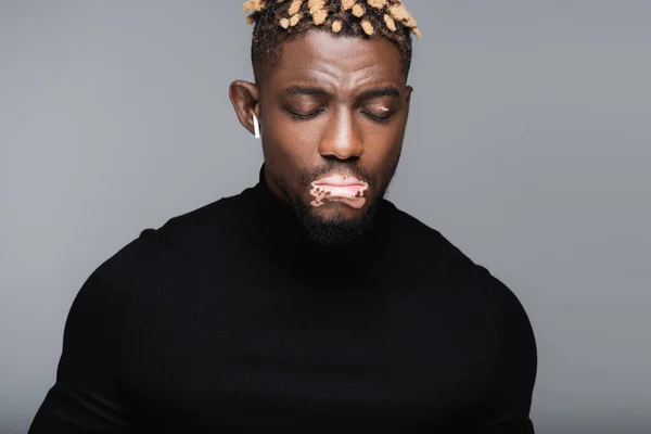 African american man with vitiligo skin listening music in earphone with closed eyes isolated on grey — Photo de stock