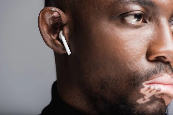 Close up view of cropped african american man with vitiligo listening music in earphone isolated on grey — Photo de stock