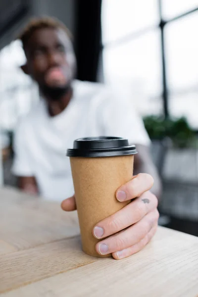 Selective focus of paper cup in hand of blurred african american man with vitiligo in office — Stock Photo