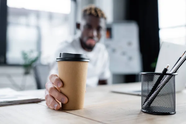 Selective focus of takeaway drink in hand of african american man with vitiligo skin in office — Stockfoto