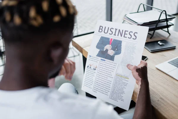 Blurred african american man with vitiligo reading business newspaper near notebook and gadgets in office — Photo de stock