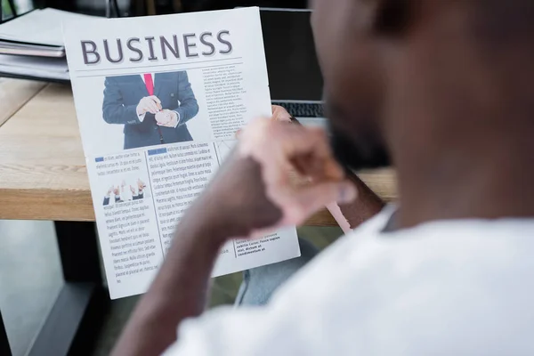 Cropped view of blurred african american man with vitiligo skin reading business newspaper in office — Photo de stock