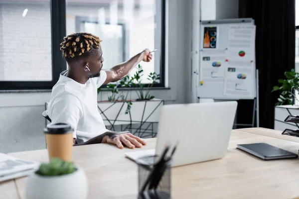 African american man with vitiligo pointing at graphs on flip chart during video call in office — Fotografia de Stock