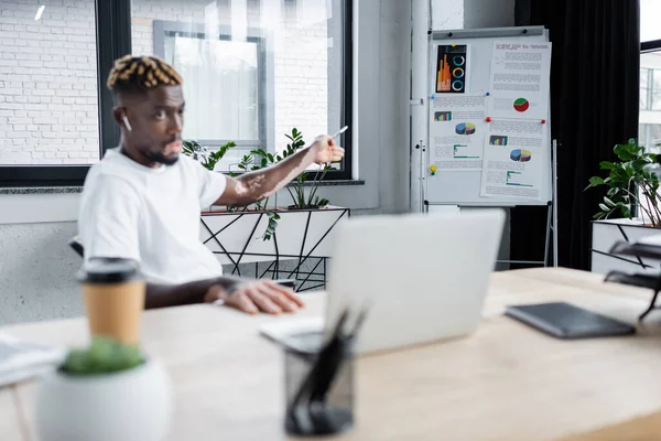 Blurred african american man with vitiligo pointing at infographics on flip chart during video call on laptop — Stock Photo