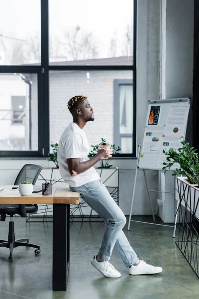 Вид збоку афроамериканця з вітіліго, що стоїть з кавою, щоб піти ближче до фліп-чарт в офісі — стокове фото