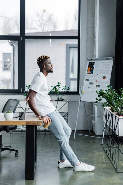 Вид збоку афроамериканця зі шкірою вітіліго, що стоїть на навушниках біля столу та розмитою фліп-чарт — стокове фото