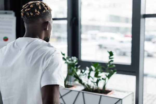 Back view of african american man with trendy hairstyle listening music in earphone in office — Photo de stock
