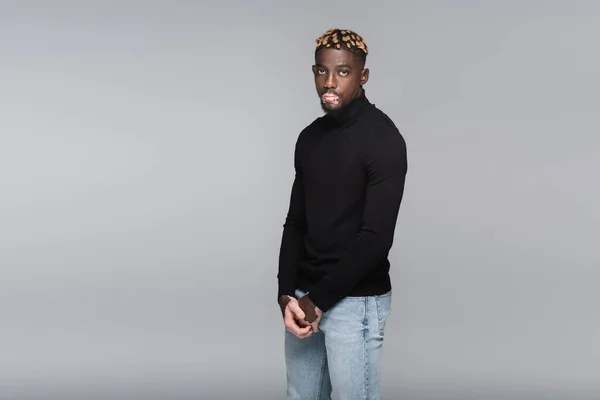 Trendy african american man with vitiligo standing in black turtleneck and jeans isolated on grey — Fotografia de Stock
