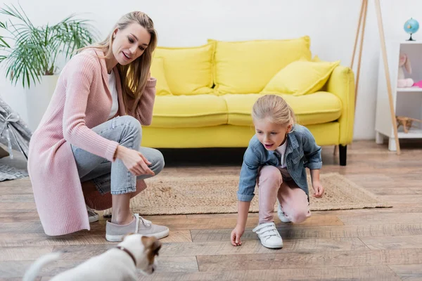 Smiling kid looking at blurred jack russell terrier near mother at home — Stockfoto