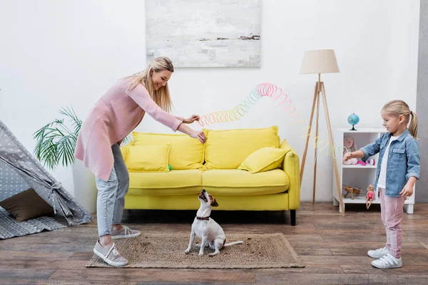 Smiling mom and kid holding colorful slinky near jack russell terrier at home — Foto stock