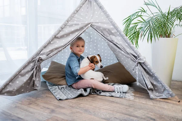 Kid hugging jack russell terrier in tepee at home — Stock Photo