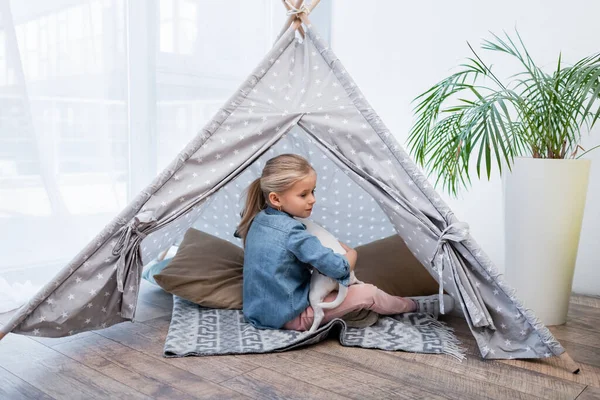 Girl hugging jack russell terrier in teepee near plant at home — Stock Photo