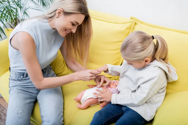 Усміхнена мати і дитина грають з лялькою на дивані вдома — стокове фото