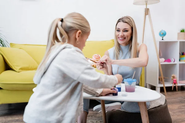 Smiling woman looking at blurred daughter painting at home — стоковое фото