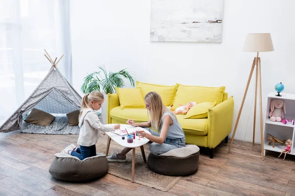 Side view of woman sitting near kid drawing on sketchbook at home — Fotografia de Stock