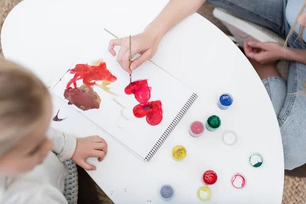 Overhead view of woman drawing heart sign near blurred daughter at home — Stock Photo