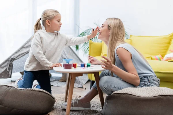 Smiling kid with hand in paint touching mom near gouache at home — Photo de stock