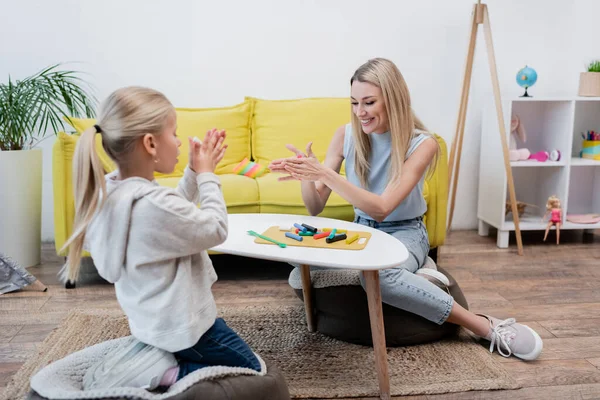 Smiling woman warming plasticine near blurred kid at home — стоковое фото