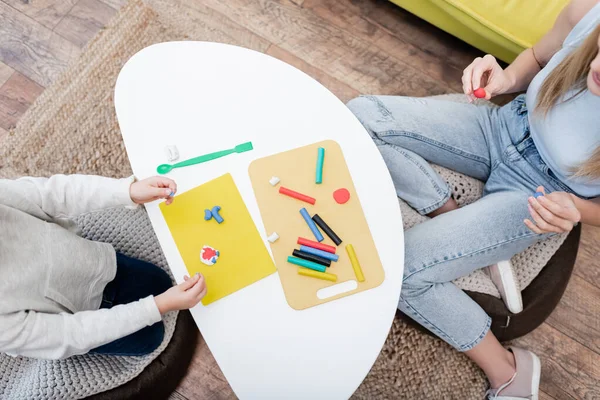 Top view of mother and kid holding plasticine near coffee table at home — Fotografia de Stock